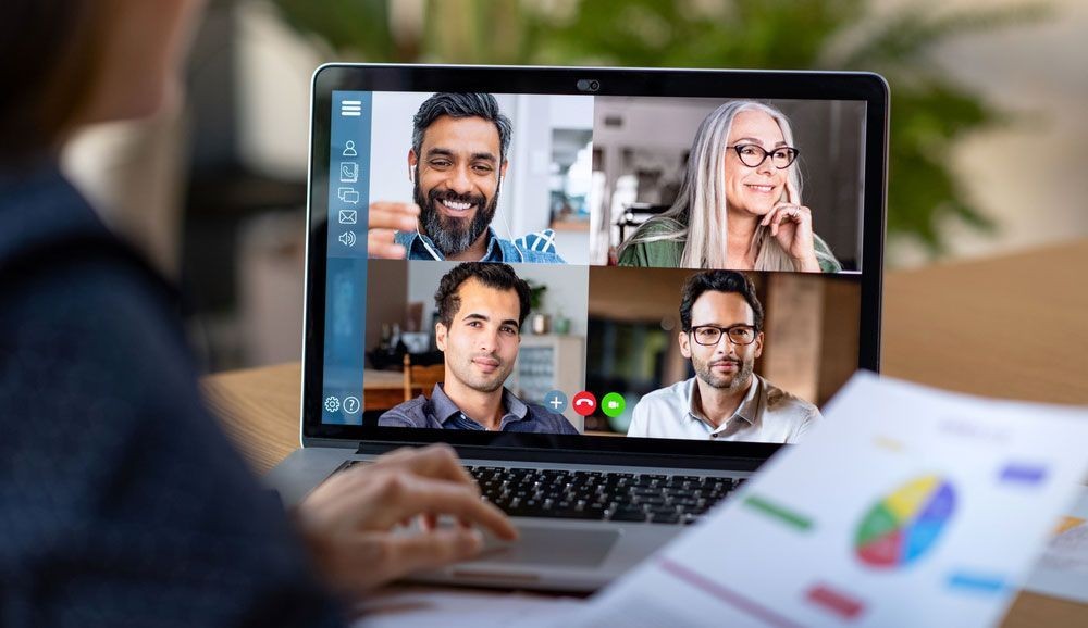 Person participating in a group video conference call on a laptop while holding a printed chart.